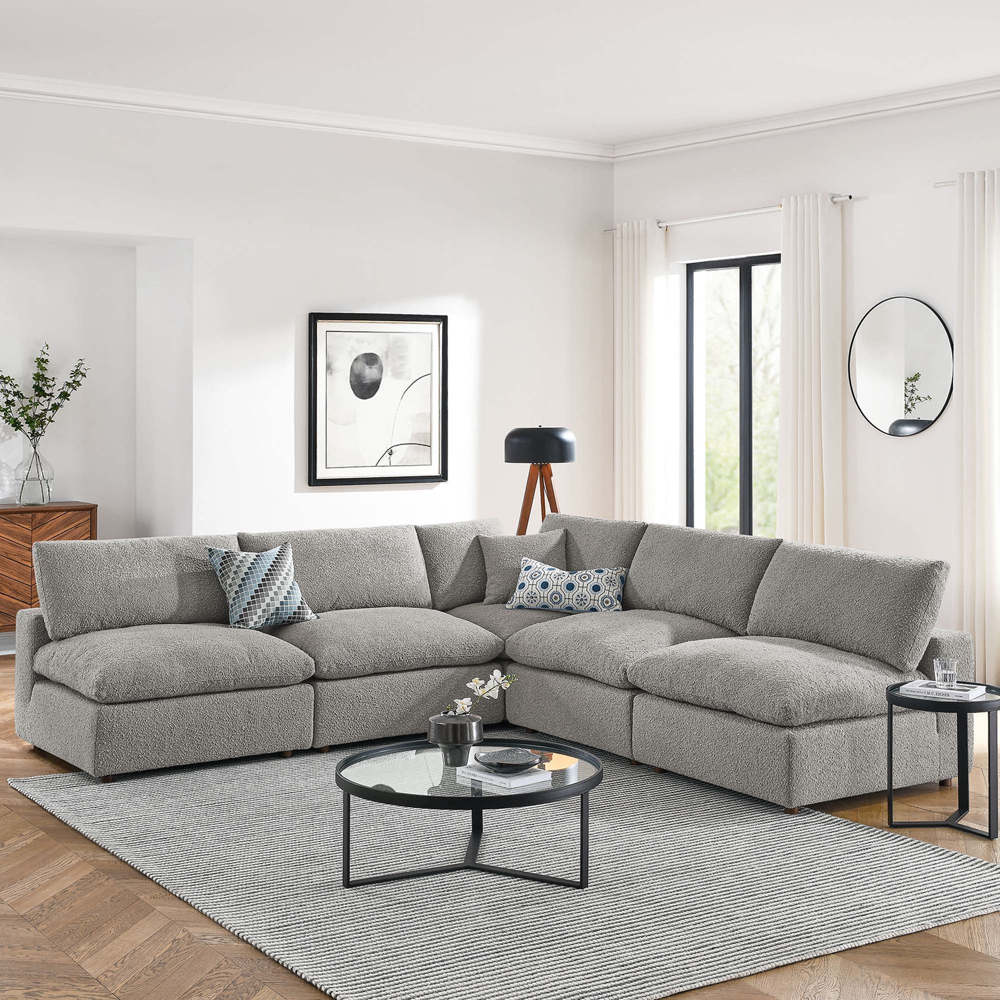 Light gray fabric L-shaped sectional sofa with plush cushions in a bright modern living room; round glass coffee table and gray rug.