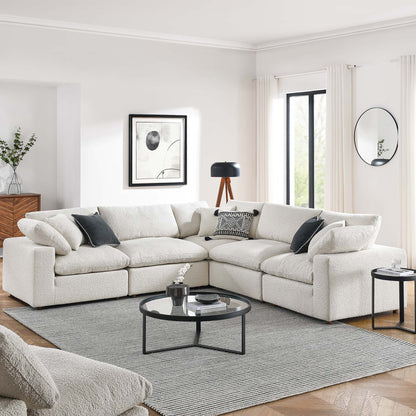 Ivory L-shaped boucle sectional sofa with dark throw pillows, round glass coffee table on gray rug in modern living room.