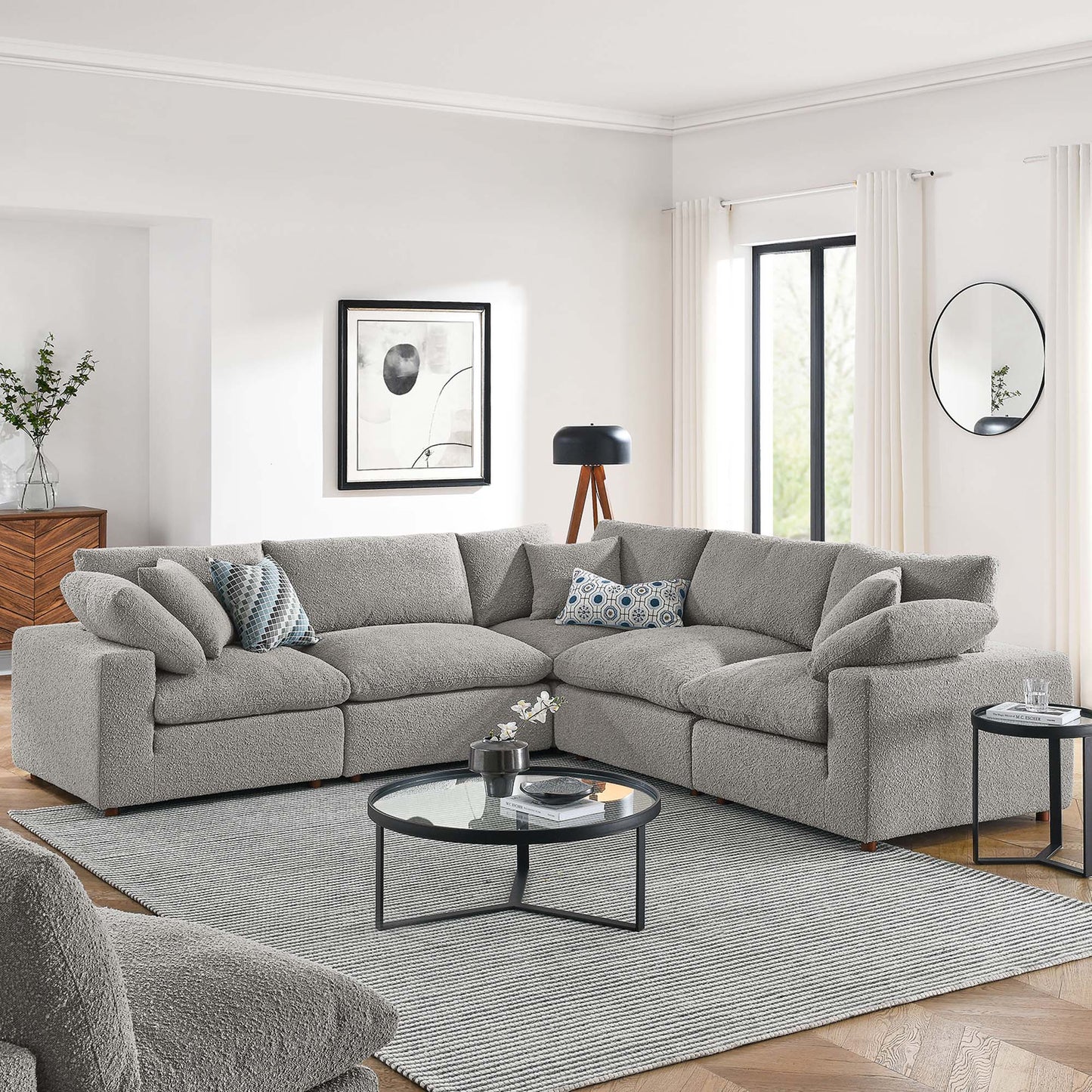 Light gray boucle sectional sofa (L-shaped) with mixed cushions, round glass-top coffee table, and gray rug in a modern living room.