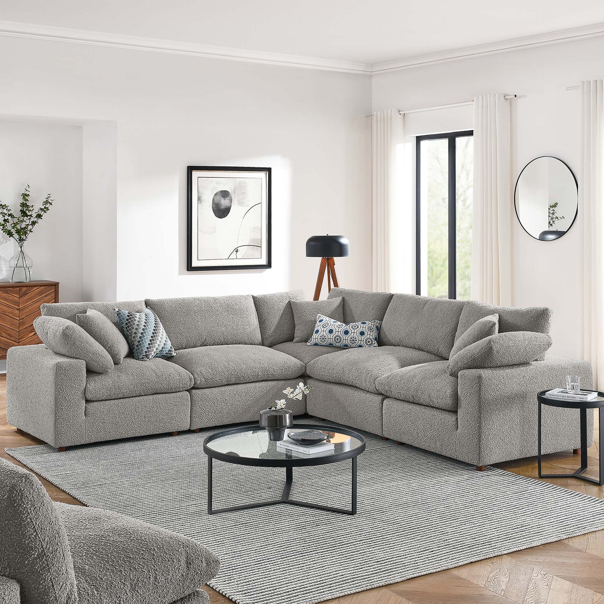 Light gray boucle sectional sofa (L-shaped) with mixed cushions, round glass-top coffee table, and gray rug in a modern living room.