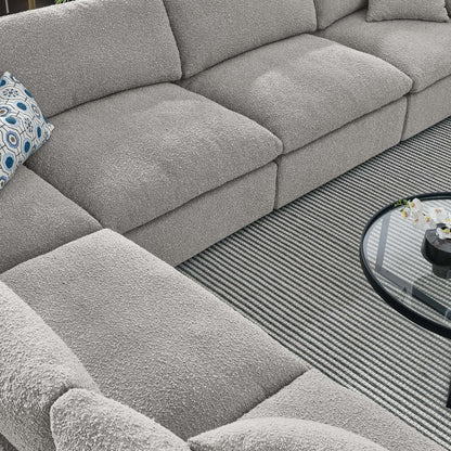 L-shaped gray boucle sectional sofa with a blue patterned pillow and round glass coffee table on a striped rug.