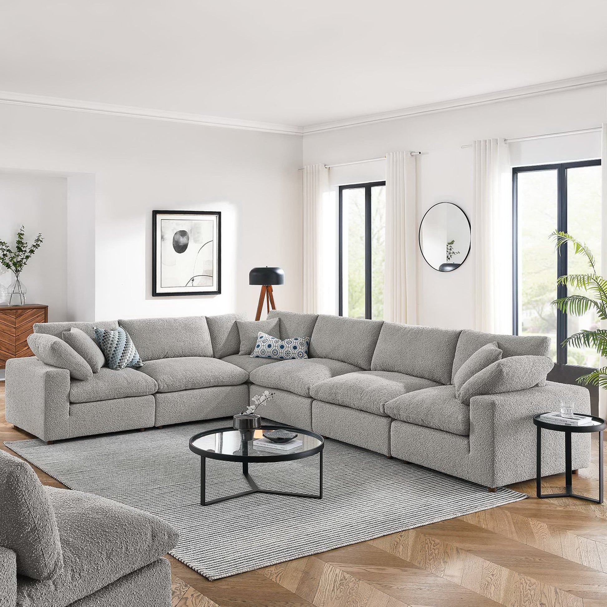 Light gray fabric L-shaped sectional sofa in a bright modern living room with a round glass coffee table on a gray rug.
