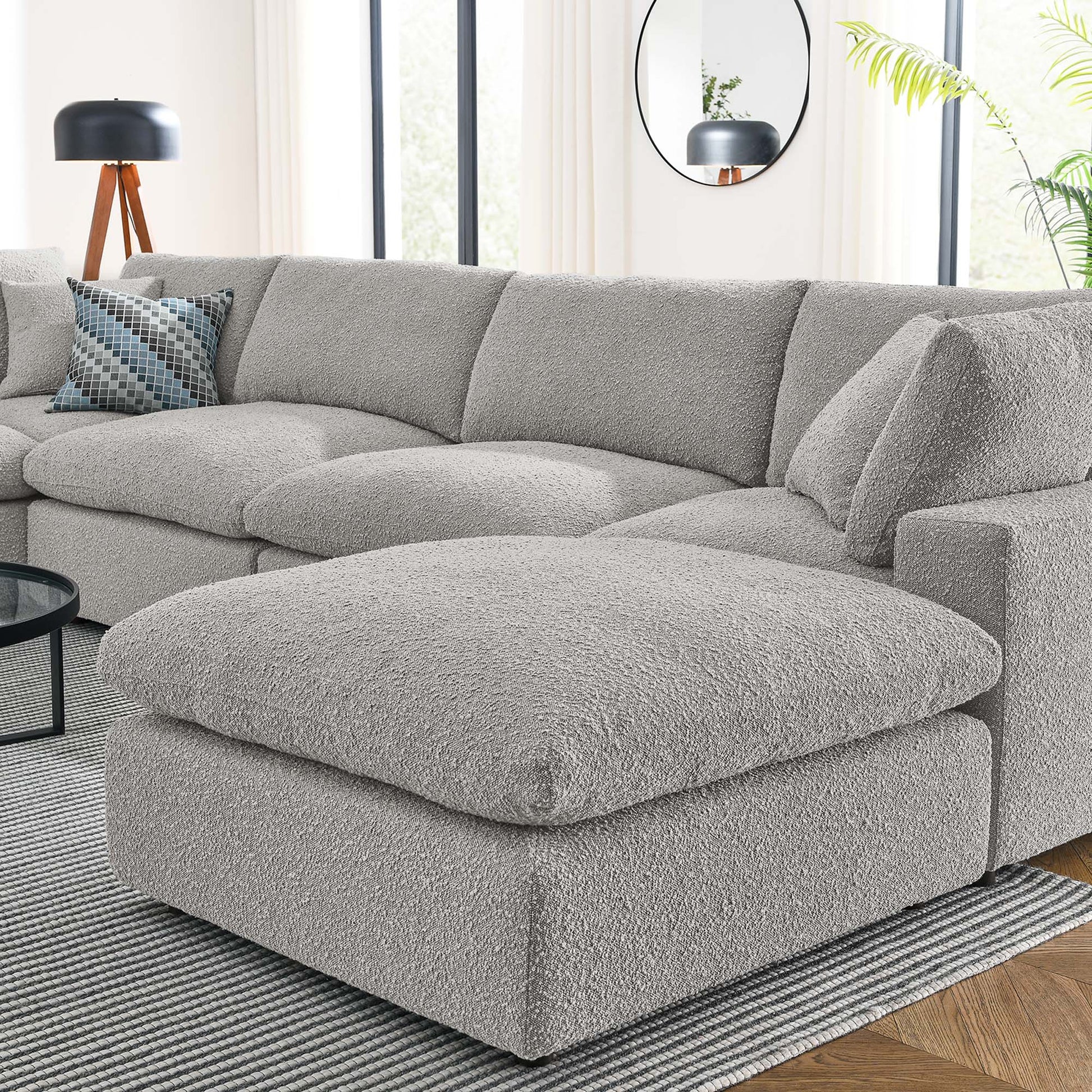 Light gray boucle sectional sofa with oversized matching ottoman in a modern living room.