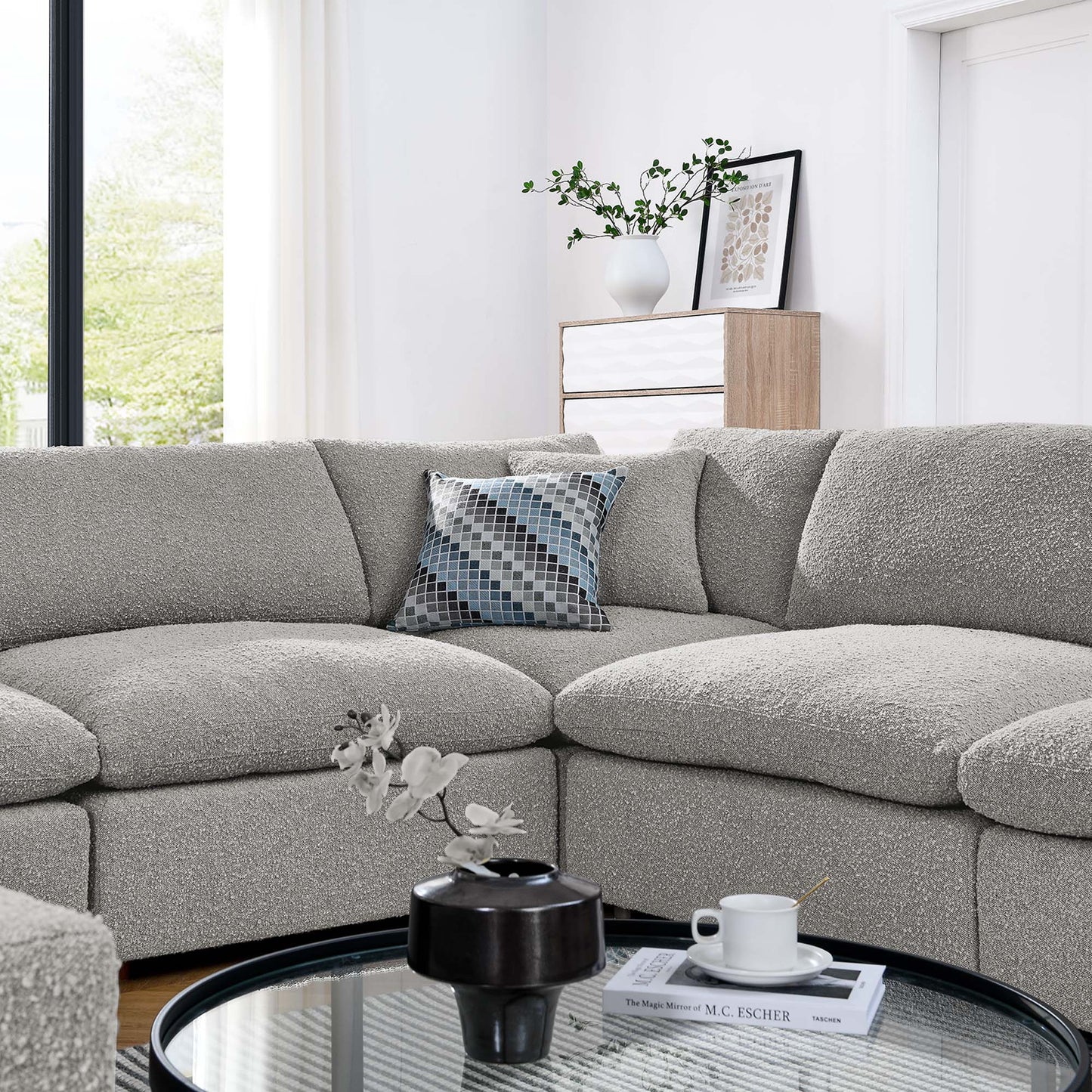 L-shaped light gray textured fabric sectional sofa with a blue geometric pillow, round glass coffee table in a modern living room.