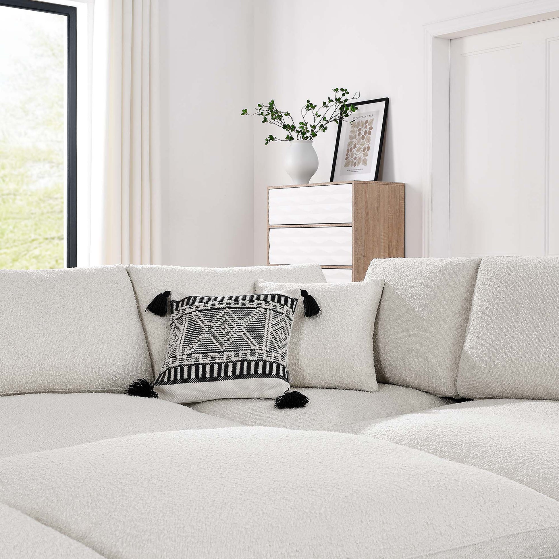 Ivory boucle sectional sofa with a black tassel-trimmed geometric pillow in a bright modern living room