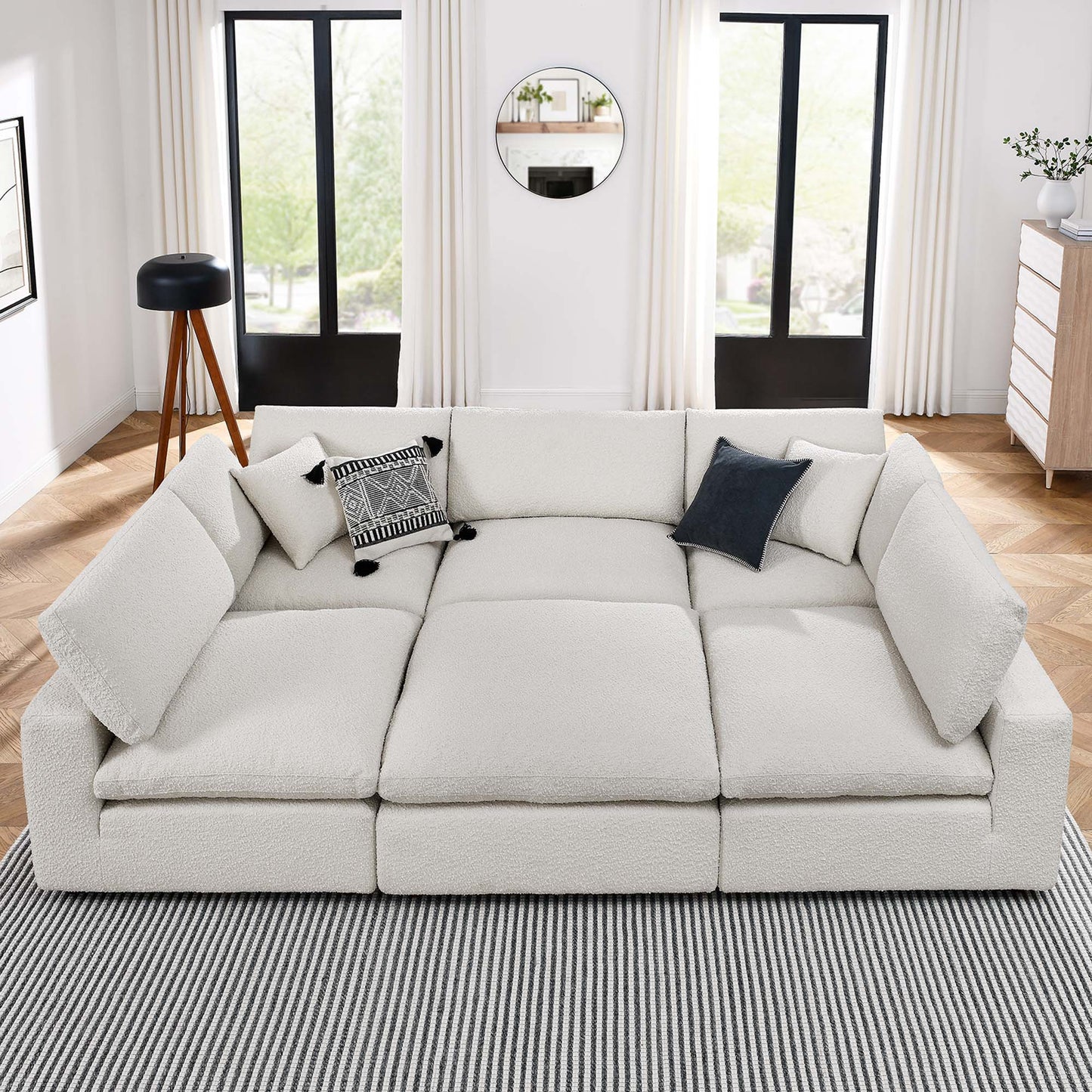 Ivory modular sectional sofa with plush cushions in a bright living room; striped rug, black-framed doors, round mirror.