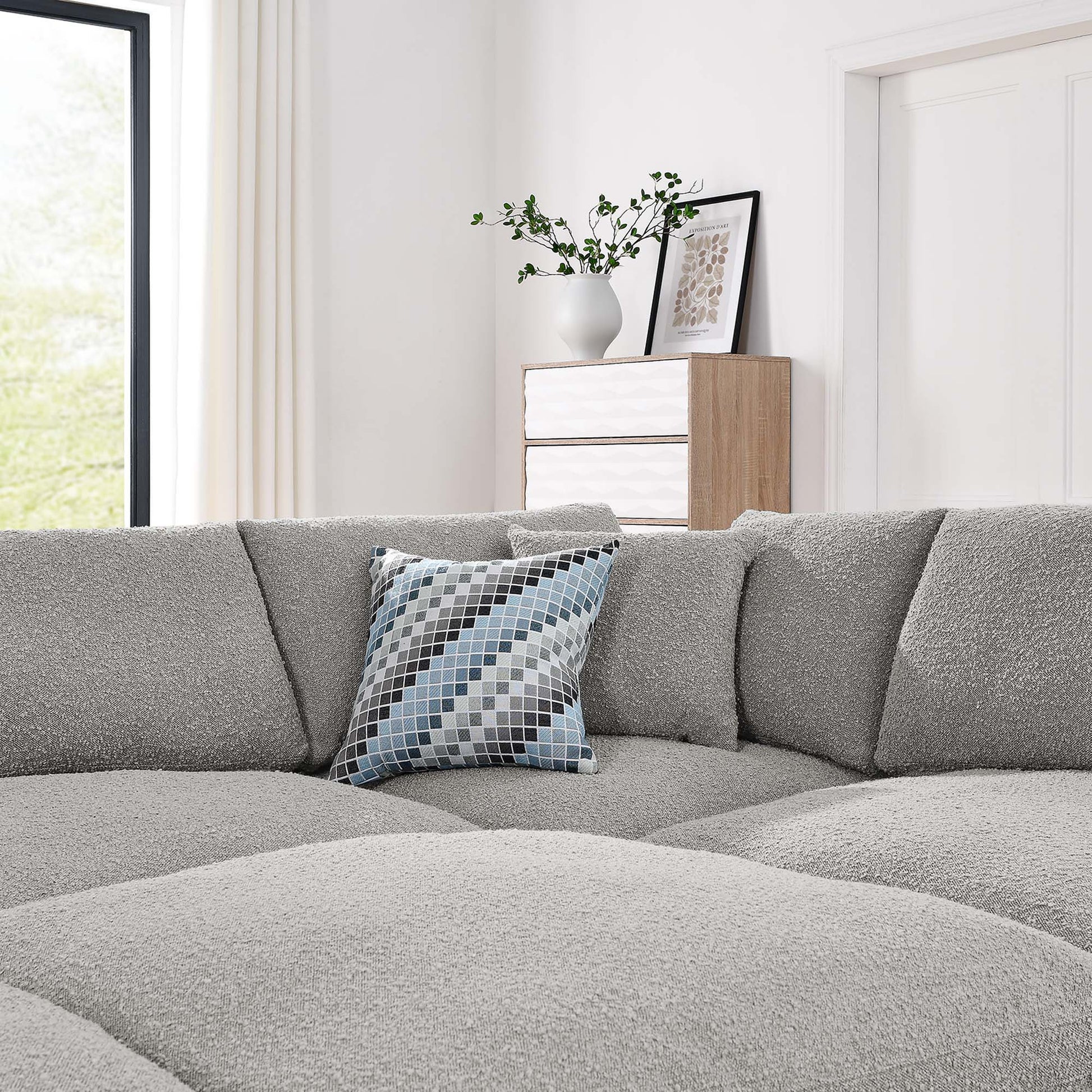 Light gray modular sectional sofa with boucle fabric and a blue-gray geometric pillow; white wood console with a vase and framed art.