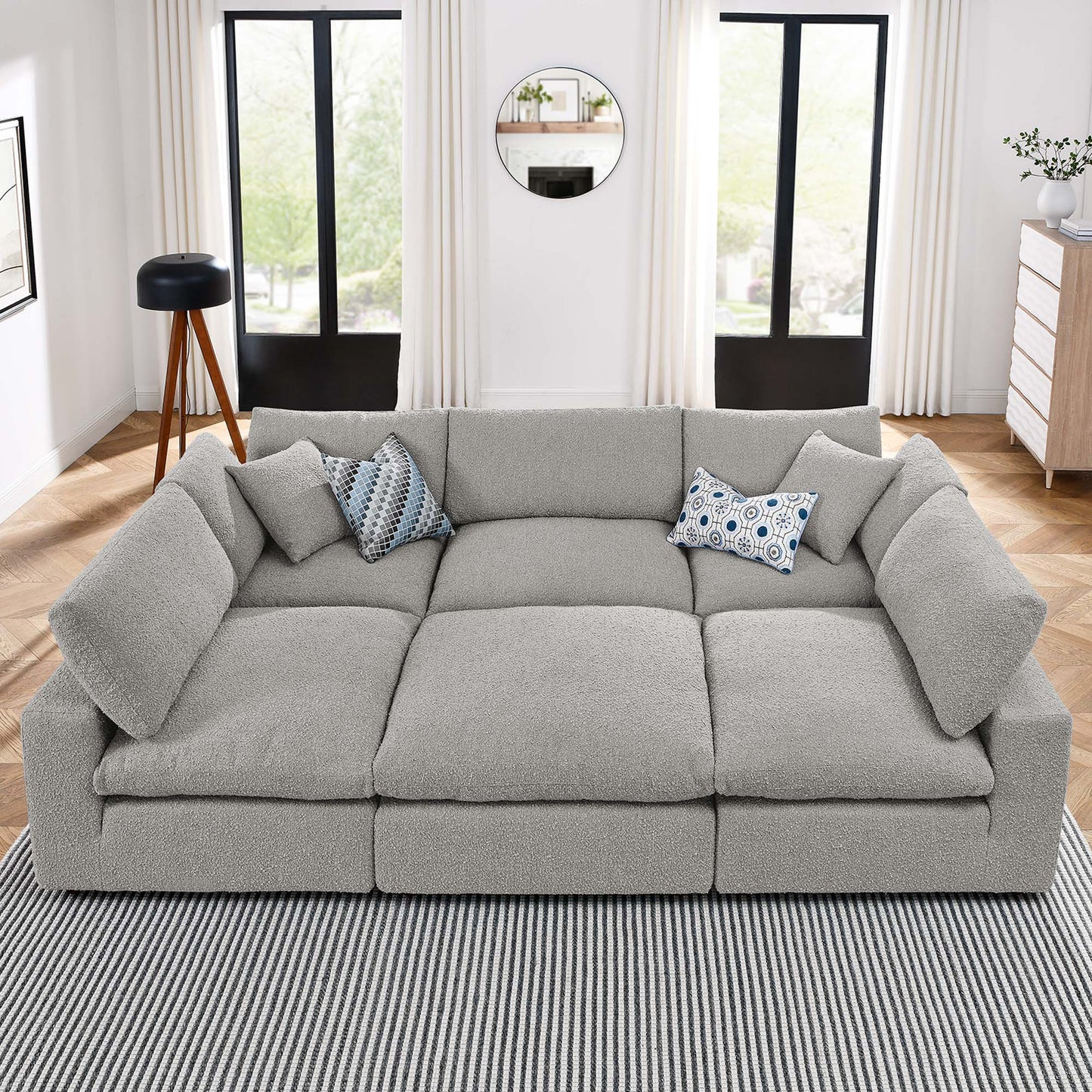 Gray fabric modular sectional sofa with deep cushions and blue patterned throw pillows in a bright living room.