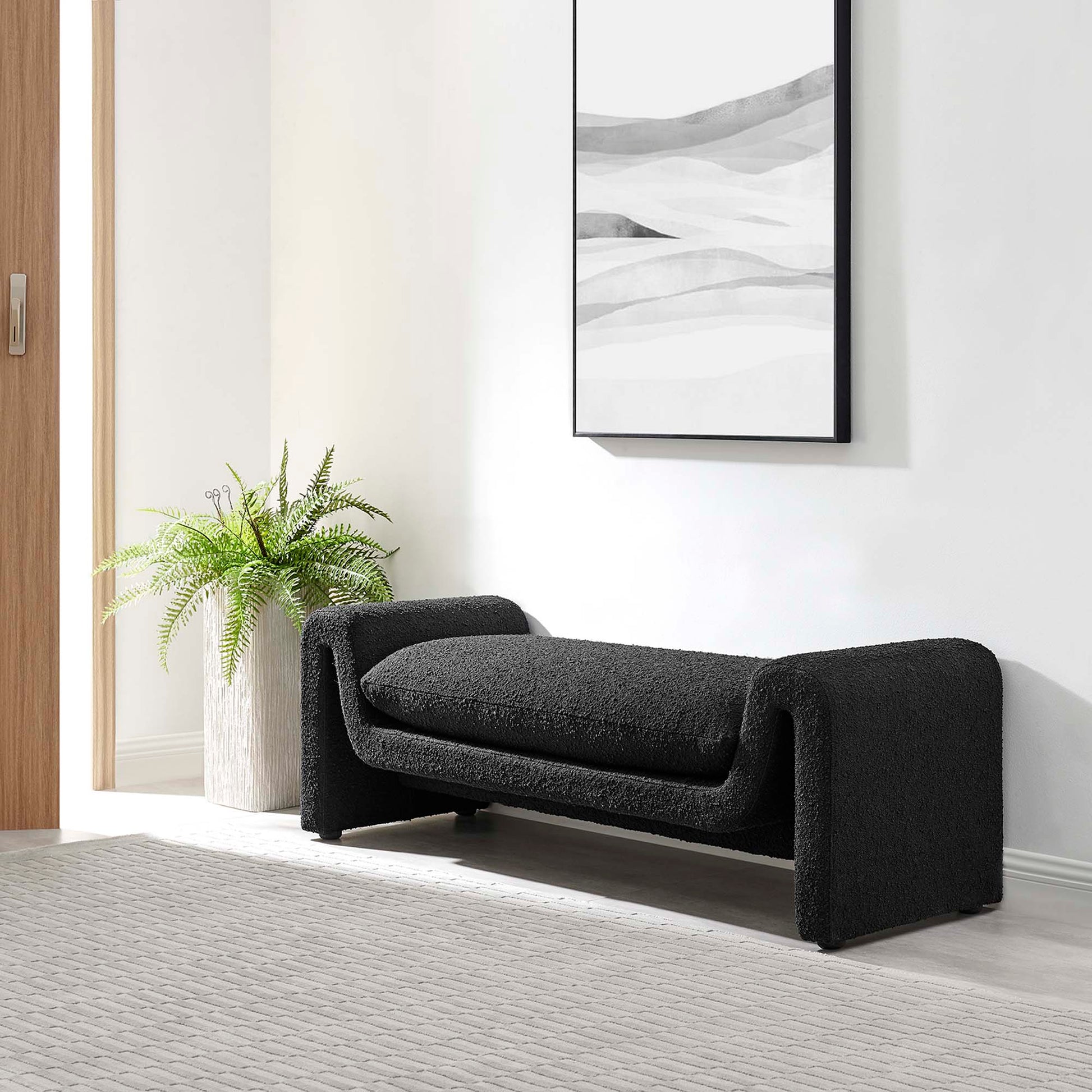 Charcoal black curved boucle fabric bench with wraparound arms in a modern entryway, with fern and abstract wall art.