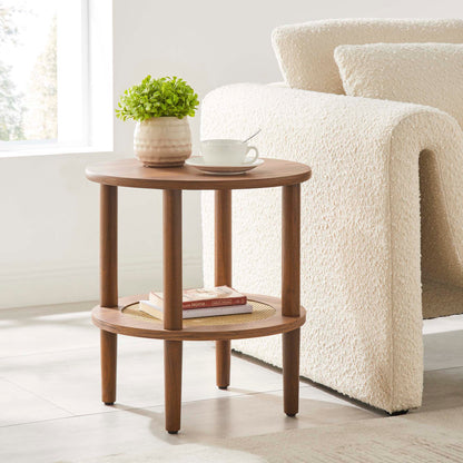 Walnut round 2-tier side table with cylindrical legs beside a cream boucle mid-century sofa; plant, cup on top.
