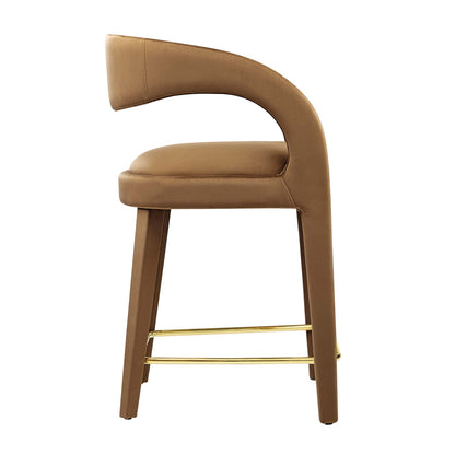 Tan-brown upholstered counter stool with a curved back, wooden legs, & gold-tone foot rails.