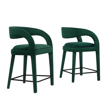 Pair of emerald green velvet counter stools with curved back arms and black metal footrests.