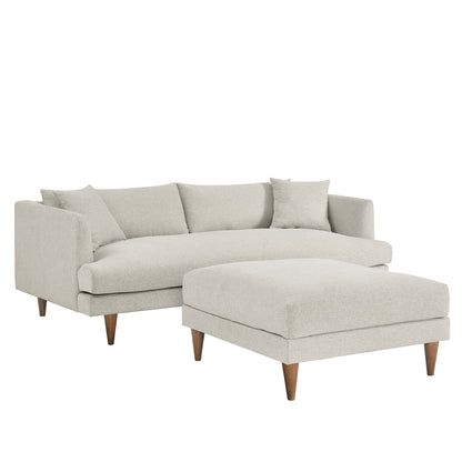 White fabric sectional sofa with matching ottoman, mid-century wooden legs, and throw pillows.