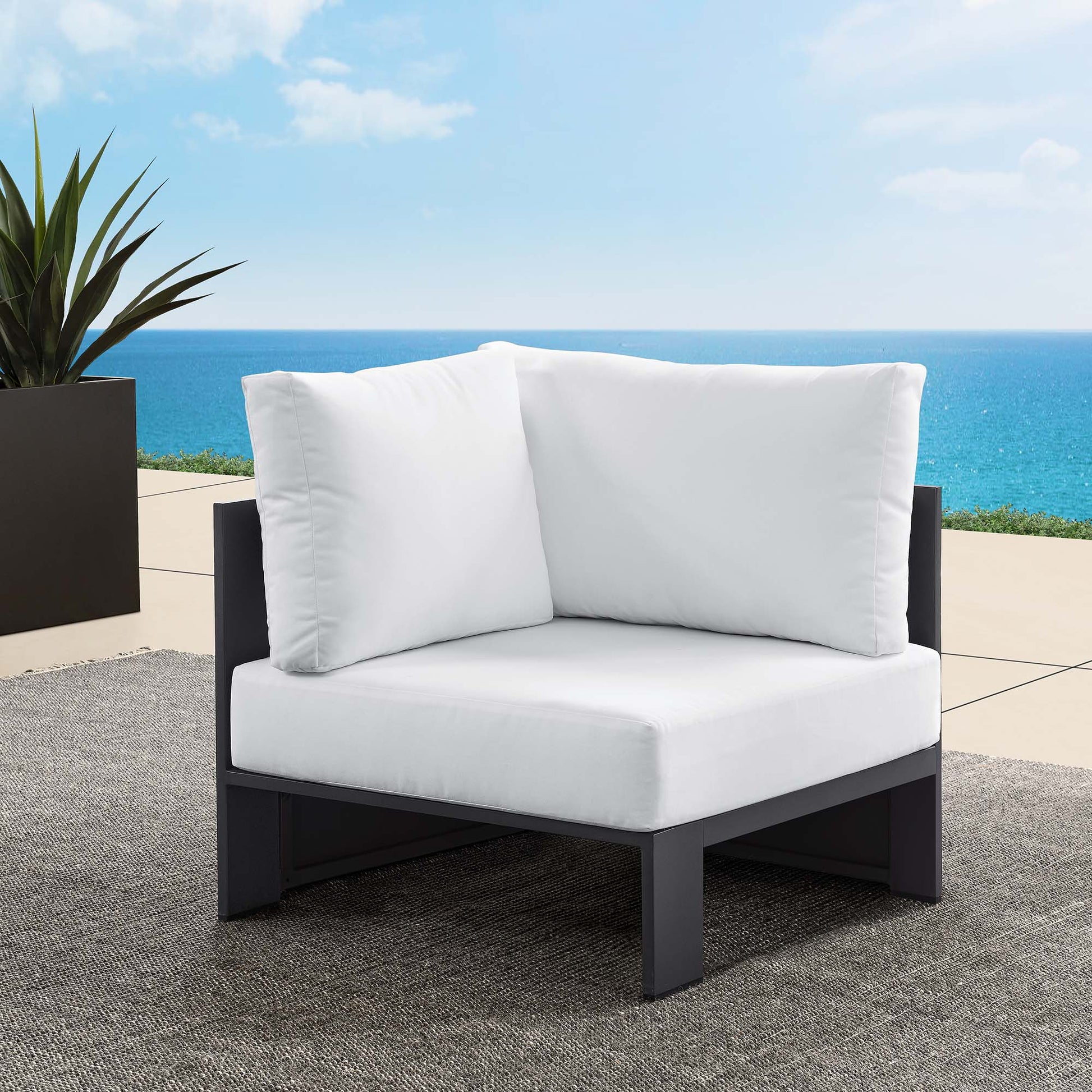 Outdoor modular corner chair with white cushions and a powder-coated aluminum frame on a seaside patio.