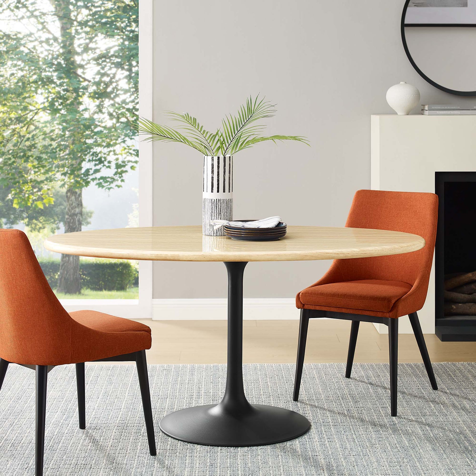 Oval faux travertine dining table on a black tulip pedestal, orange upholstered chairs, vase with greenery in a modern dining room.