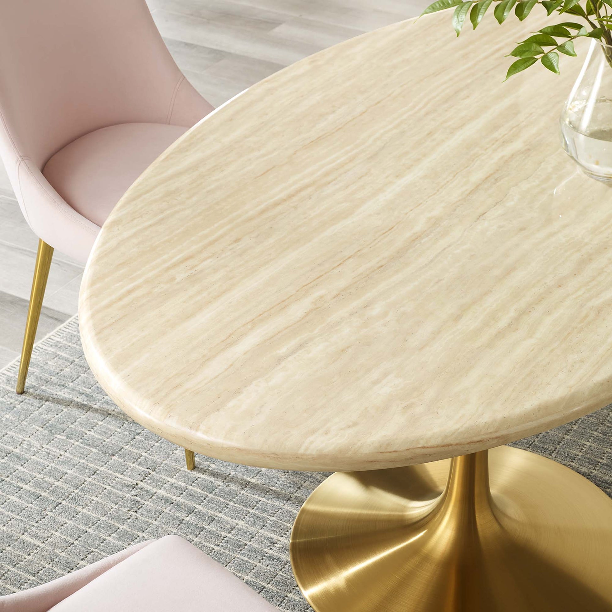 Beige faux travertine oval dining table on a gold pedestal base, with pink velvet chairs nearby.