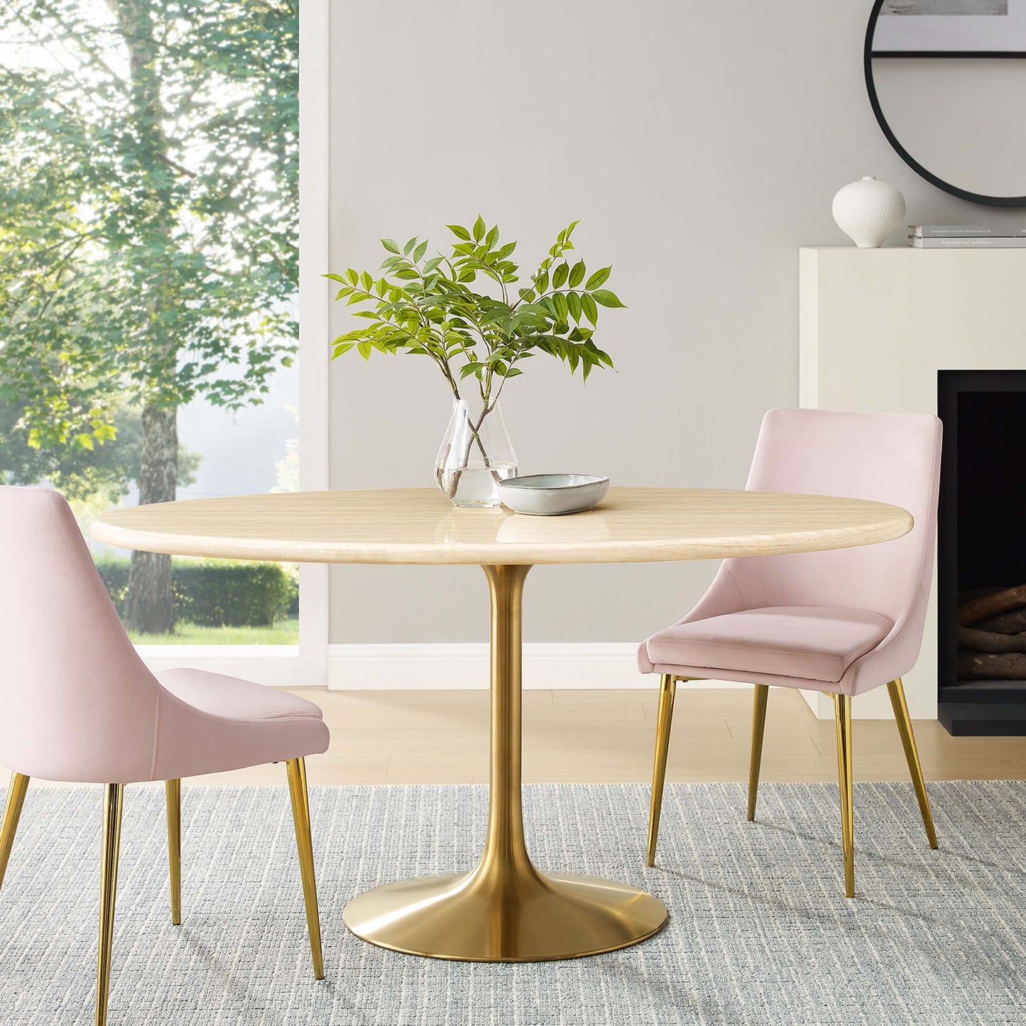 Oval faux travertine dining table with a gold tulip pedestal, surrounded by pink upholstered chairs in a modern dining room.