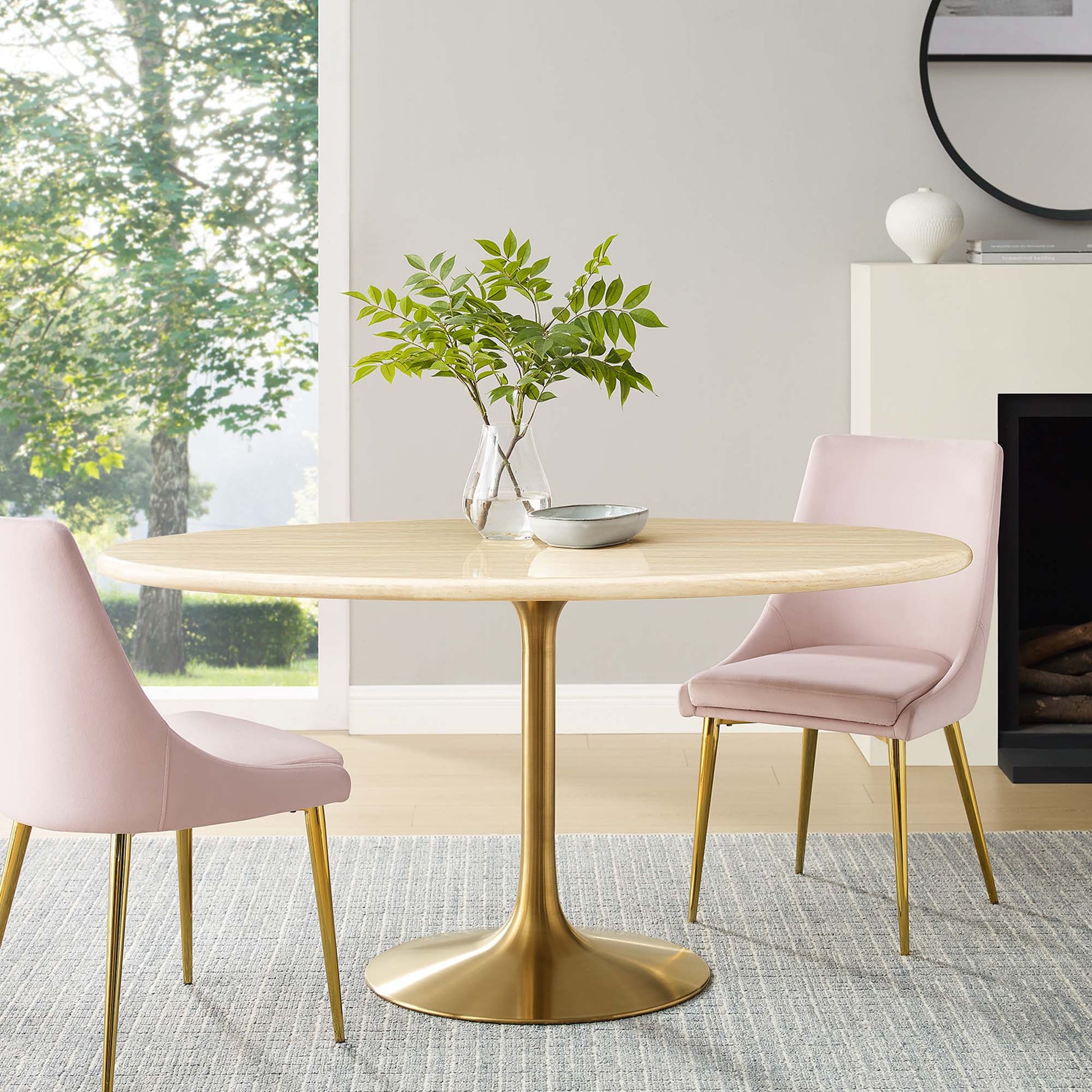 Oval faux travertine dining table with a gold tulip pedestal, surrounded by pink upholstered chairs in a modern dining room.
