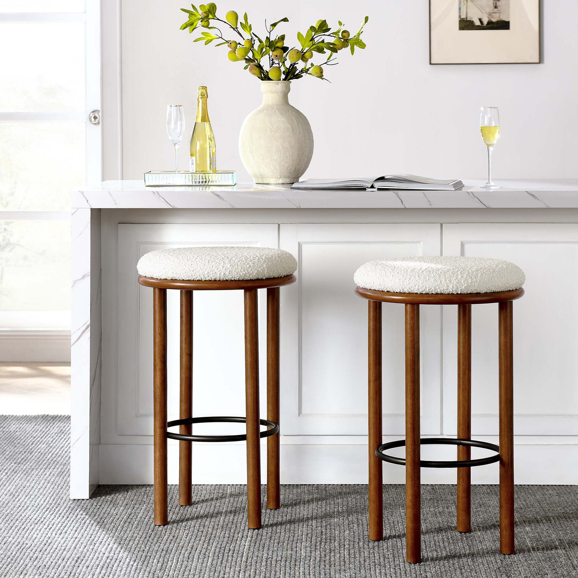 Two walnut wood bar stools with ivory boucle fabric seats and metal foot rings beside a white marble kitchen island