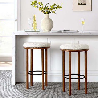 Two walnut wood bar stools with ivory boucle fabric seats and metal foot rings beside a white marble kitchen island