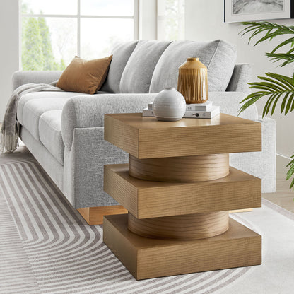 Modern living room with a gray sofa and a stacked wooden pedestal side table with a round base, vase, books, beige pillow.
