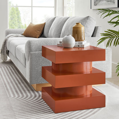 Glossy red stepped end table with chunky square shelves beside a gray sofa, topped with vases and books.