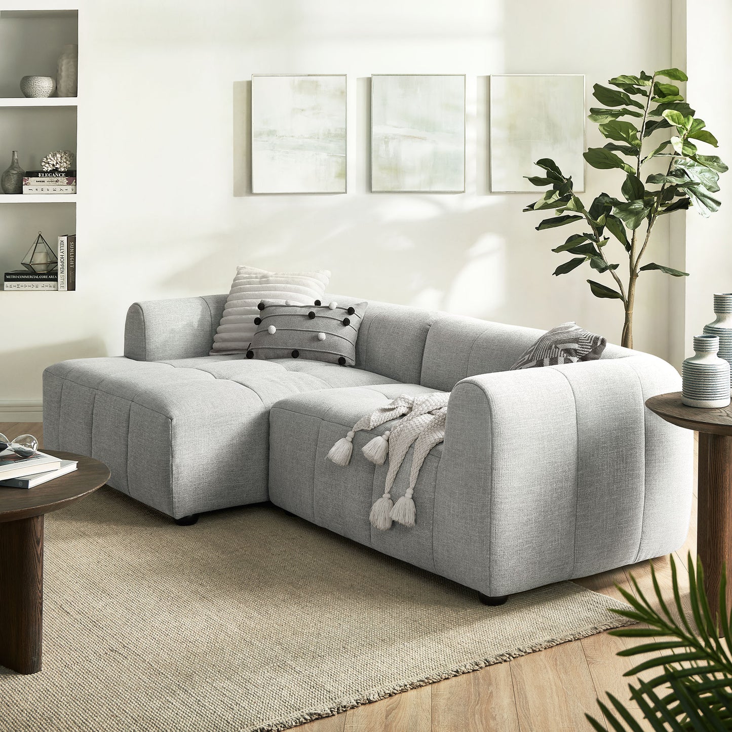 Light gray fabric sectional with chaise in a modern living room; tassel throw, striped pillow, beige rug, abstract wall art.
