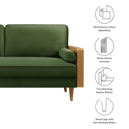 Green velvet sofa with walnut wood veneer armrests, matching bolster pillows, and wooden legs.