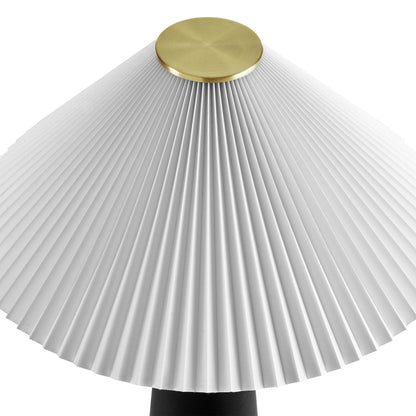 White pleated lampshade with brass cap atop a black table lamp base