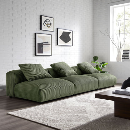 Olive green corduroy modular sofa in a white brick living room with abstract art, rug, and dark wood coffee table.