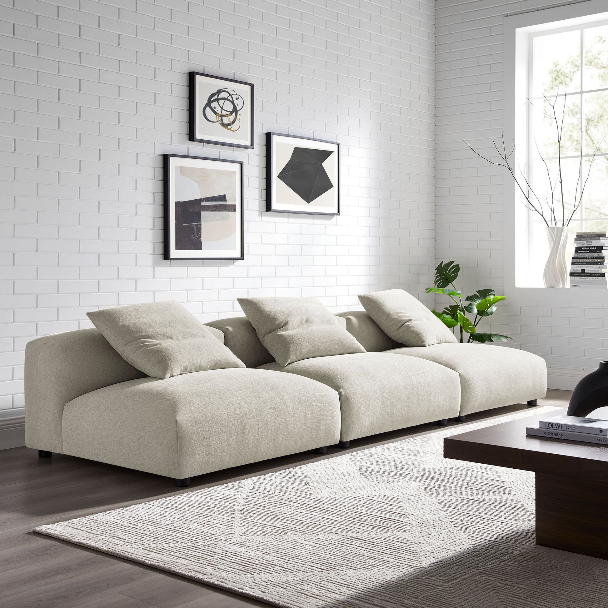 Beige linen three-seat sofa with plush cushions in a modern living room, abstract art, gray rug, dark wood coffee table.