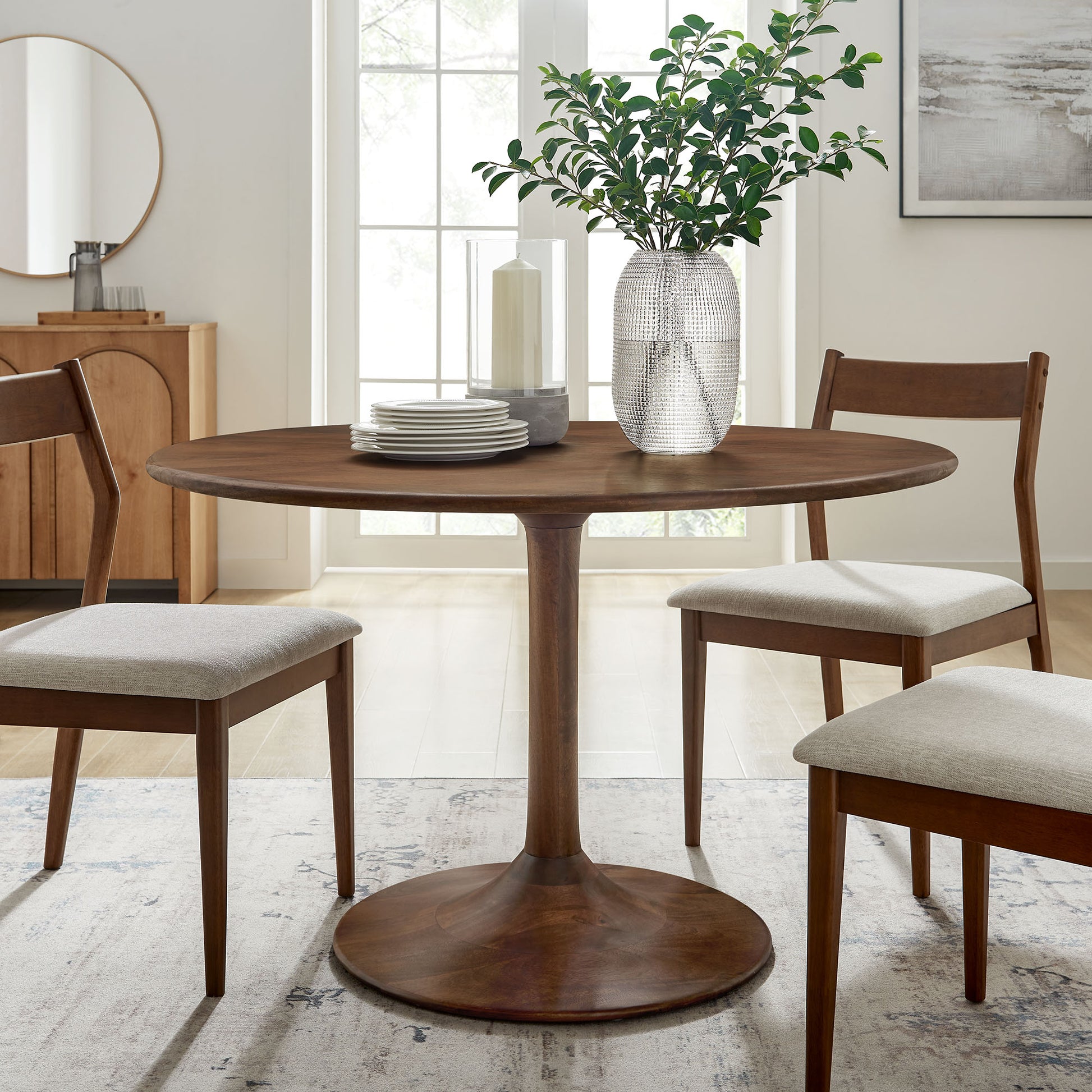 Walnut round pedestal solid wood dining table with greenery vase centerpiece.