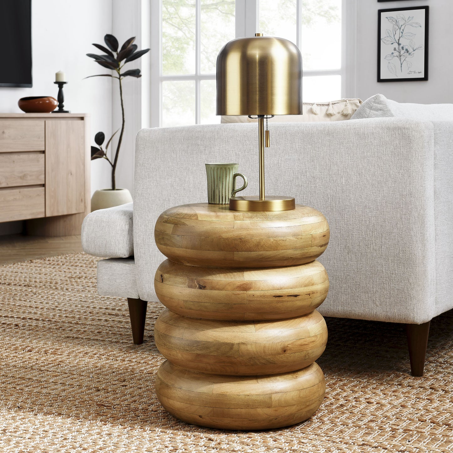 Round stacked wood side table with a natural brown finish; a green mug sits nearby.