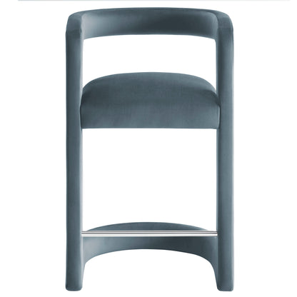 Blue velvet counter stool with a continuous curved back, cushioned seat, and chrome footrest on a wide U-shaped base.