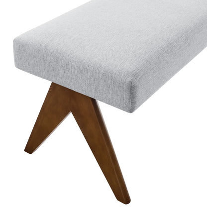 Light gray rectangular fabric upholstered bench with warm wood angled tripod legs in mid-century style, 47" long.