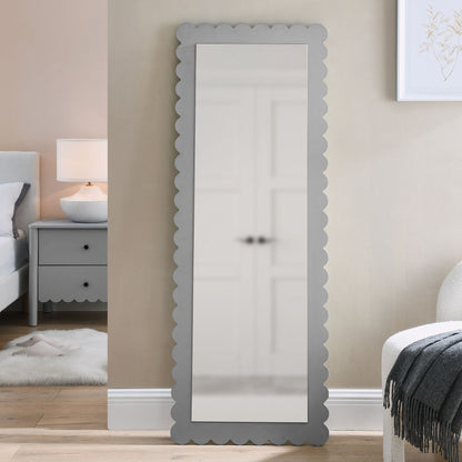 Tall full-length mirror with scalloped gray frame leaning against beige bedroom wall.