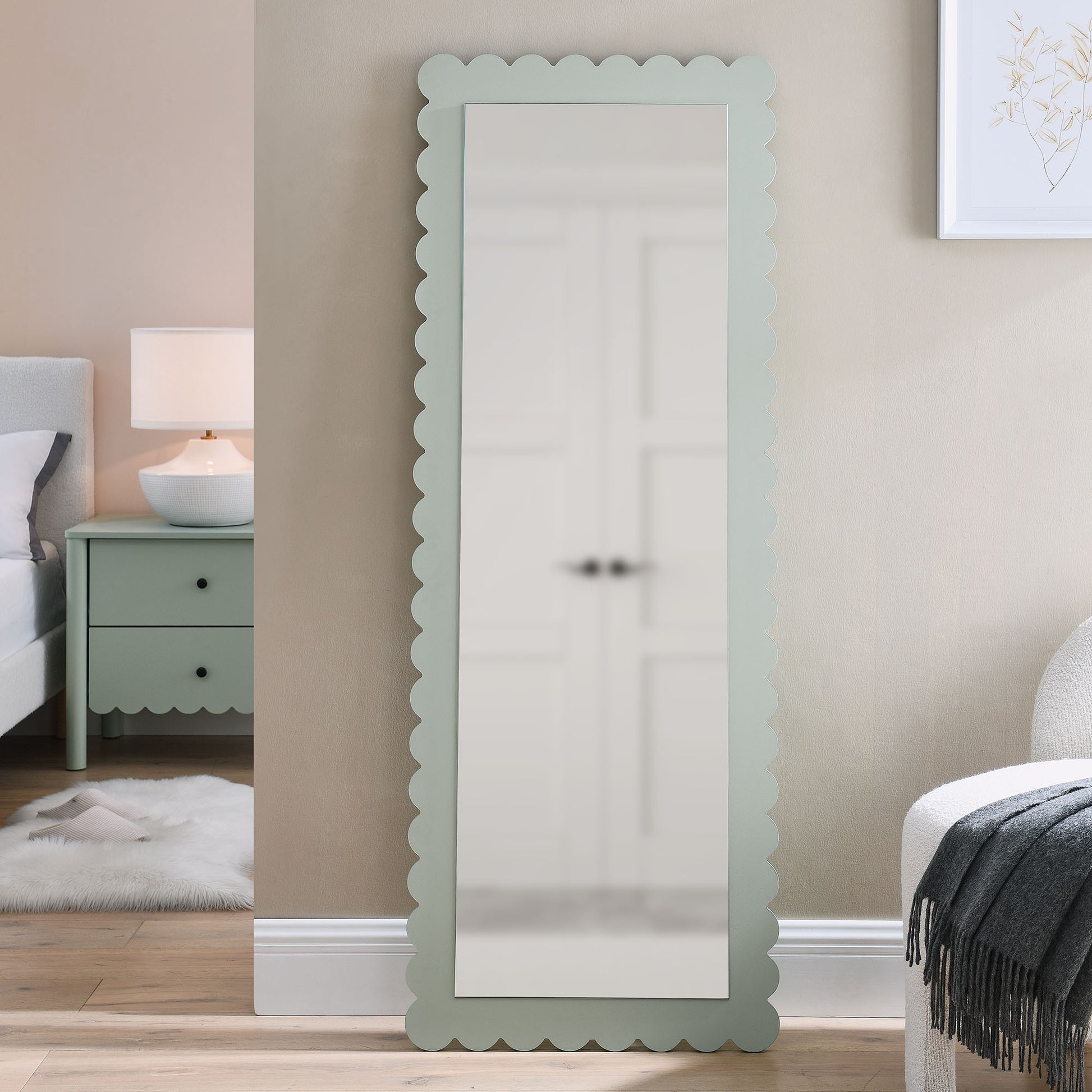 Mint green scalloped-edge wood-frame full-length mirror, leaning against a beige wall in a cozy bedroom.