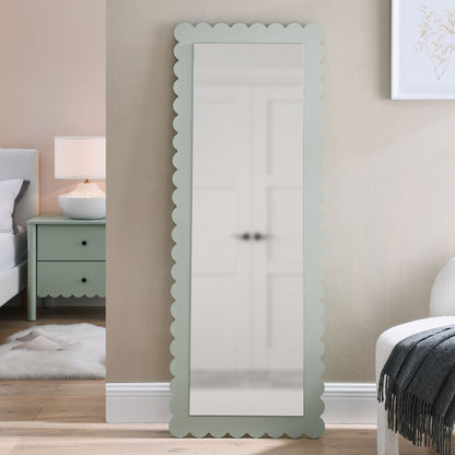 Mint green scalloped-edge wood-frame full-length mirror, leaning against a beige wall in a cozy bedroom.