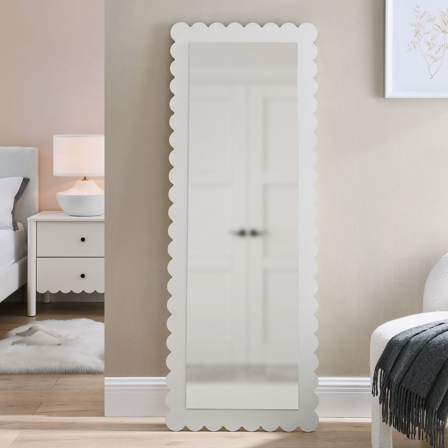 White scalloped-edge full-length mirror freestanding in a neutral-toned bedroom beside a nightstand.