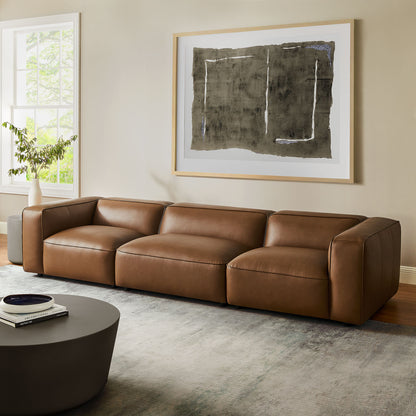 Brown vegan leather modular sofa with wide arms in a living room, abstract wall art, round coffee table, plant by window.