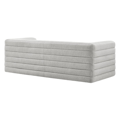 Long light gray upholstered sofa with stacked horizontal channel cushions and rounded ends.