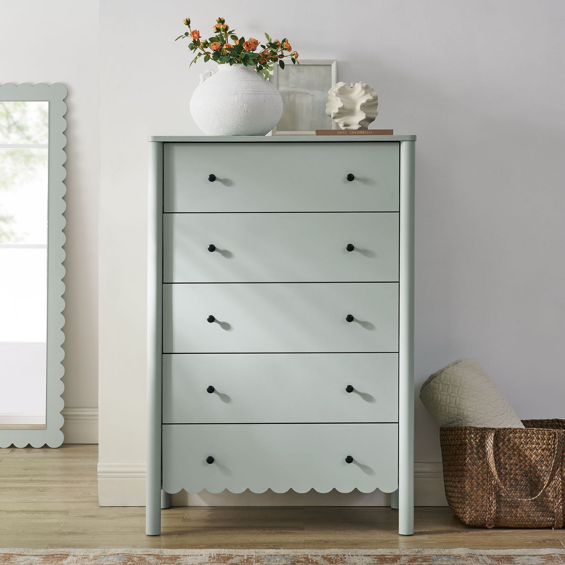 Green scalloped 5-drawer chest with black knobs, topped with a white vase of orange flowers; boho chic storage.