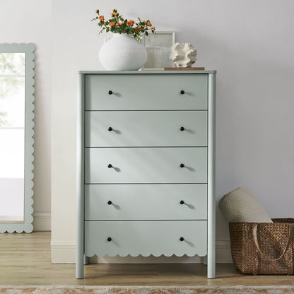 Green scalloped 5-drawer chest with black knobs, topped with a white vase of orange flowers; boho chic storage.