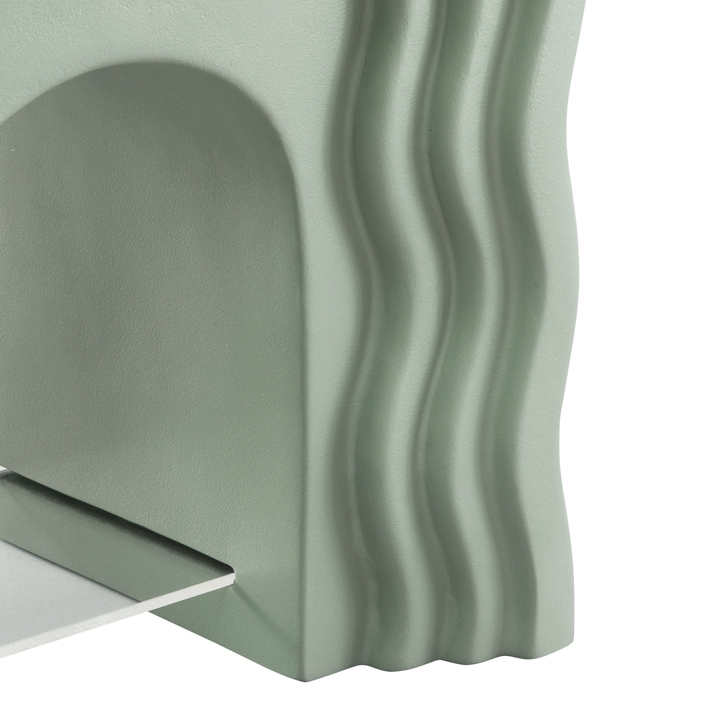 Sage green metal side table with sculptural wavy vertical ridges and a small rectangular shelf protruding.