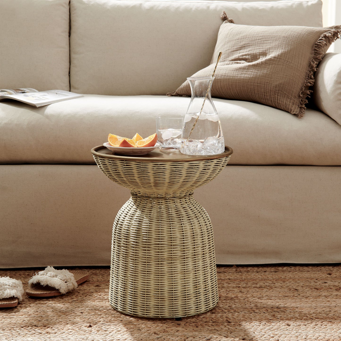Woven rattan drum side table with glass pitcher, ice and citrus slices; beige sofa with brown cushions in a cozy living room.