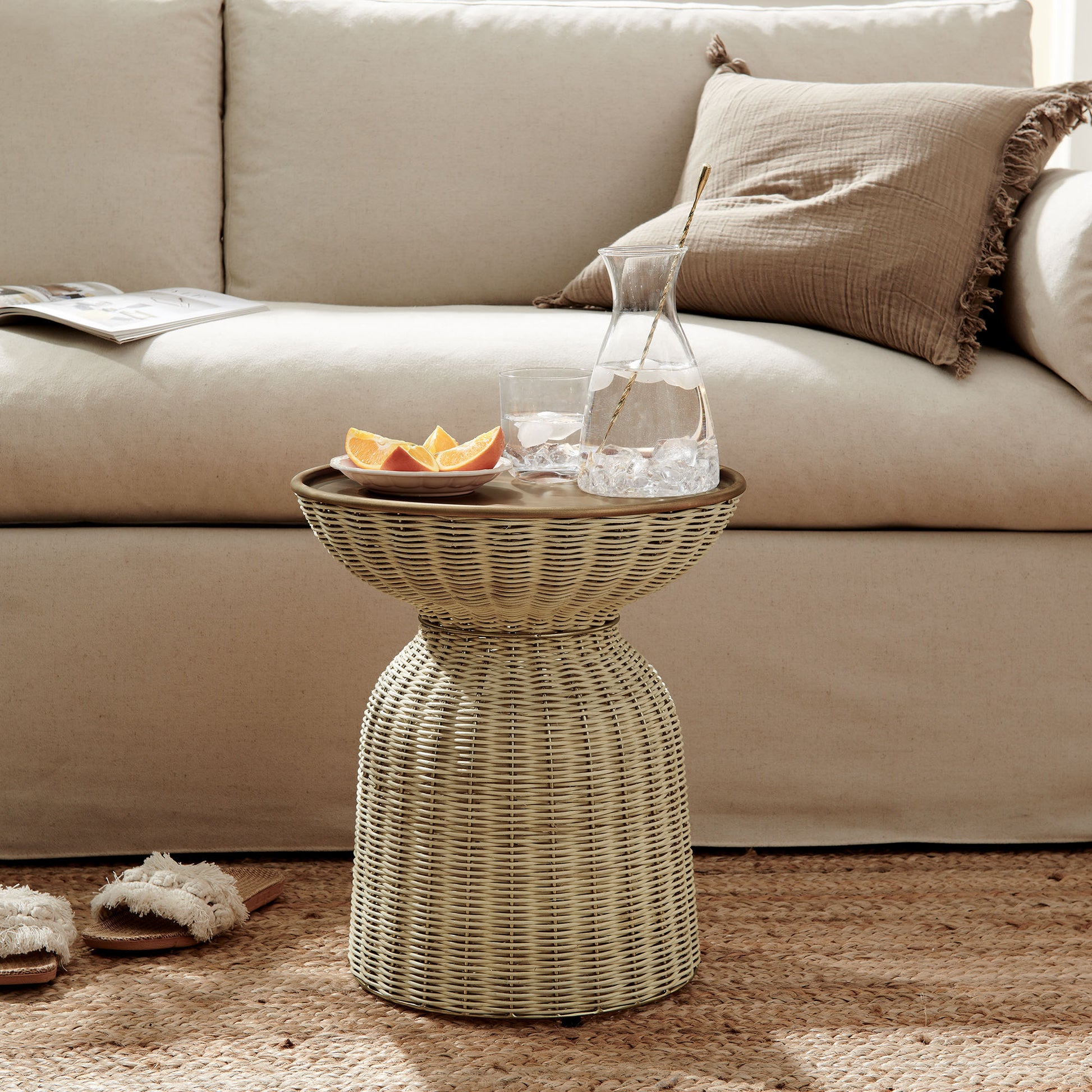 Woven rattan drum side table with glass pitcher, ice and citrus slices; beige sofa with brown cushions in a cozy living room.