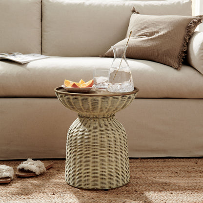 Woven rattan drum side table with glass pitcher, ice and citrus slices; beige sofa with brown cushions in a cozy living room.