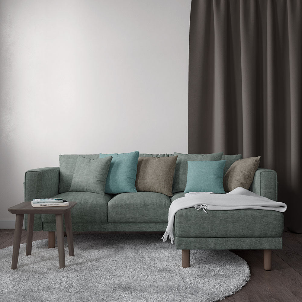 Teal-green sectional sofa with teal and taupe cushions, matching ottoman, wooden legs, white throw, gray rug.