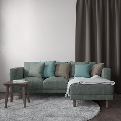 Teal-green sectional sofa with teal and taupe cushions, matching ottoman, wooden legs, white throw, gray rug.