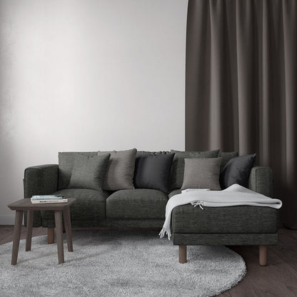 Charcoal-gray sectional sofa with matching cushions, white throw, wooden legs, on a light rug beside dark curtains.